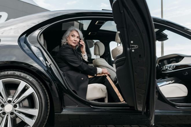 Confident senior woman sitting in a black luxury car, exuding elegance and success.