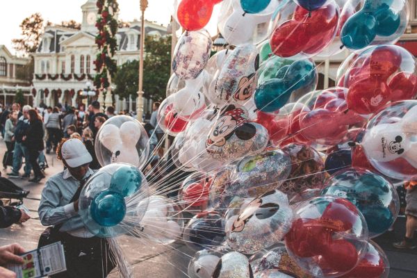 Colorful Mickey and Minnie balloons at a bustling theme park street.