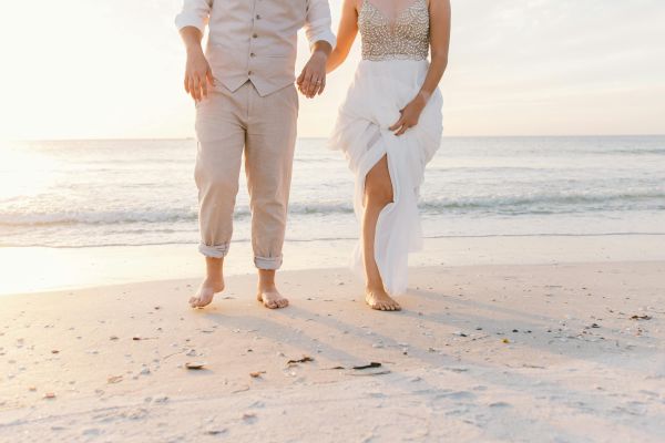 A couple walks hand in hand on a sunny beach. Perfect wedding moment captured.