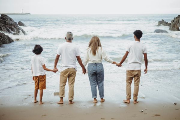 A family of four holds hands while facing the ocean, enjoying a peaceful day at the beach.