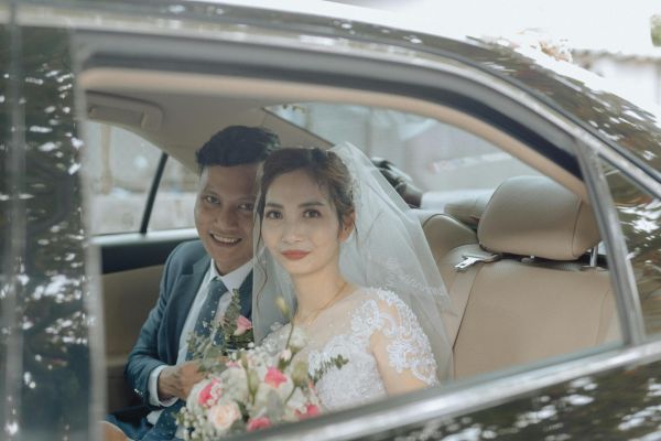 Bride and groom sitting in a car holding a bouquet, radiating happiness on their wedding day.