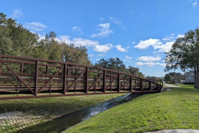 A rustic footbridge spans a quiet stream under a clear blue sky in Kissimmee, Florida.