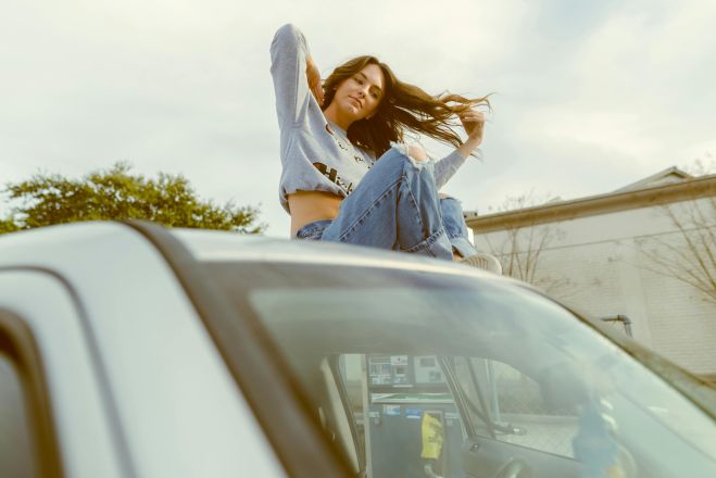 A fashionable woman sitting on a car roof in Orlando, showcasing a vibrant, carefree style